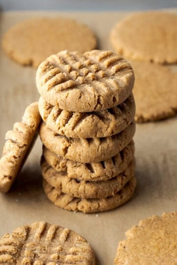 A stack of six peanut butter powder cookies on a parchment-lined baking sheet.