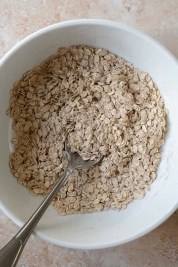 Oats, whole grain flour, and cinnamon stirred in a mixing bowl.