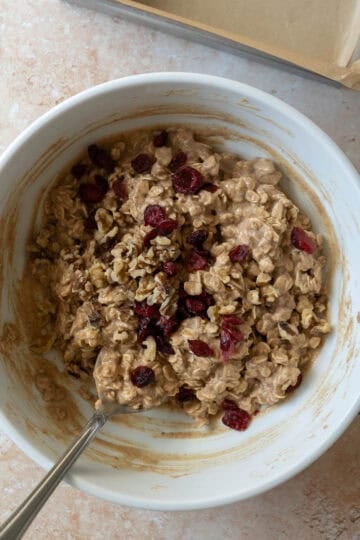 Folding dried cranberries and walnuts into the oatmeal bars batter.