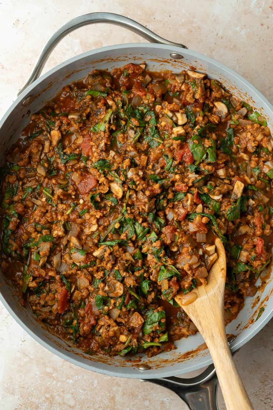 Simmering marinara with plant-based beef crumbles, aromatics, and spinach.