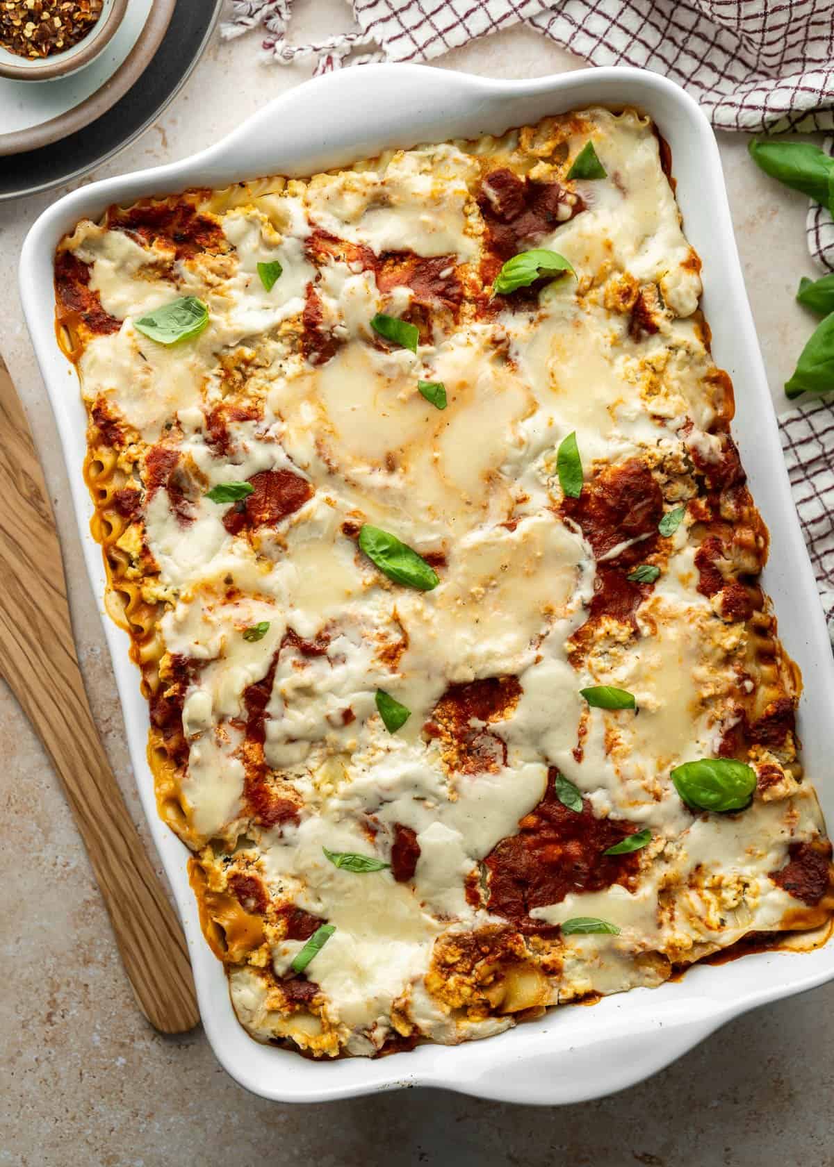 Vegan lasagna fresh from the oven with melted cheese on top and garnished with fresh basil leaves.