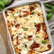 Vegan lasagna in a white casserole dish topped with two kinds of gooey, melted vegan mozzarella cheese.