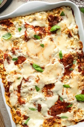 Vegan lasagna in a white casserole dish topped with two kinds of gooey, melted vegan mozzarella cheese.