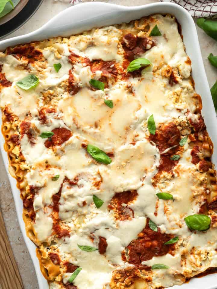 Vegan lasagna in a white casserole dish topped with two kinds of gooey, melted vegan mozzarella cheese.
