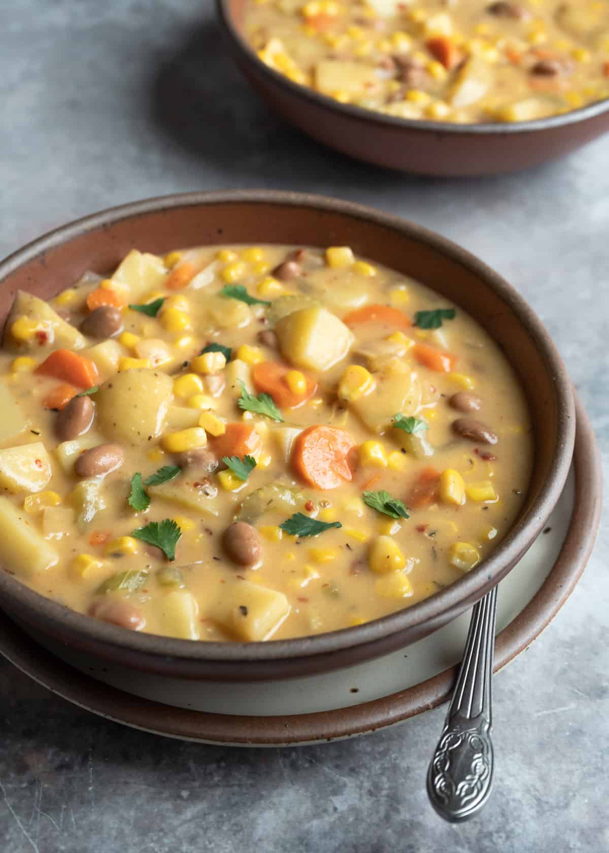 Two bowls of creamy corn and potato soup on a gray background.