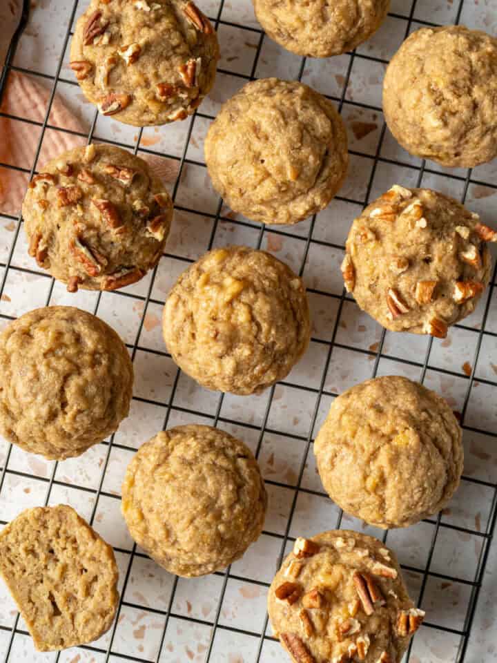 Oat flour banana muffins lined up on a cooling rack with one cut in half to show texture.