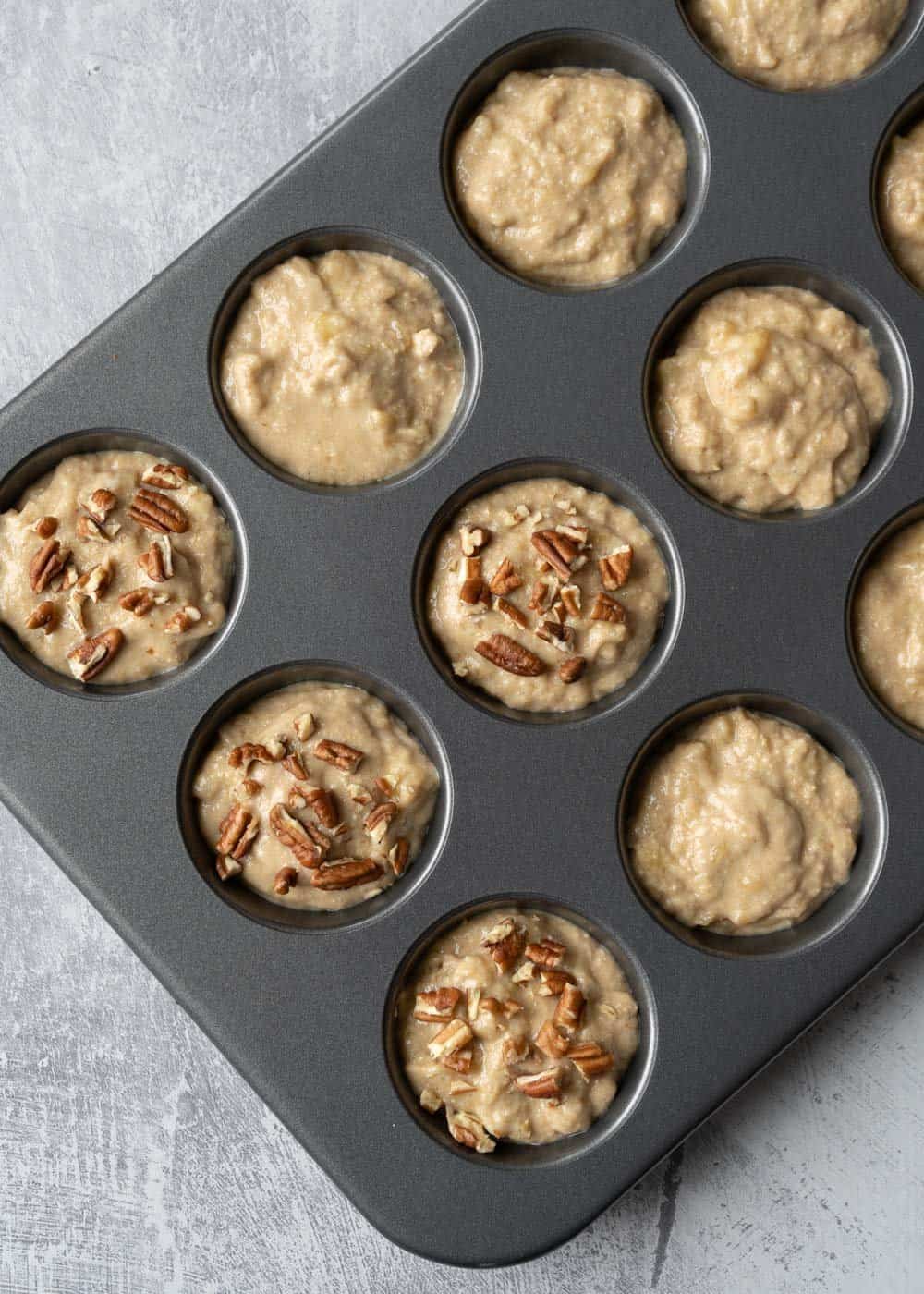 Oat flour banana muffin batter in a muffin tin with chopped nuts sprinkled on top of a few.