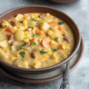Close up of a bowl of creamy vegan corn soup showing texture, colorful veggies, and potato.