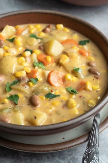 Close up of a bowl of creamy vegan corn soup showing texture, colorful veggies, and potato.