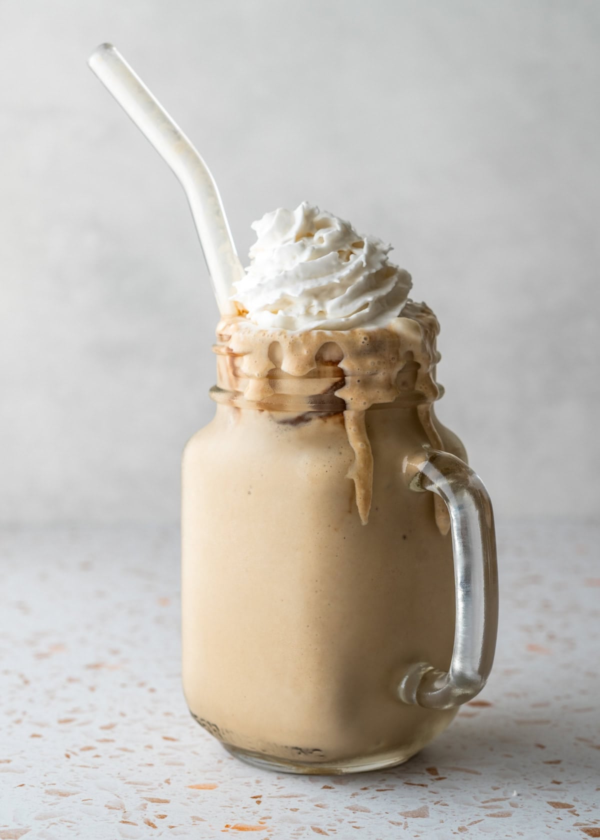 A frosty glass of homemade coffee frappuccino garnished with chocolate syrup and vegan whipped cream.