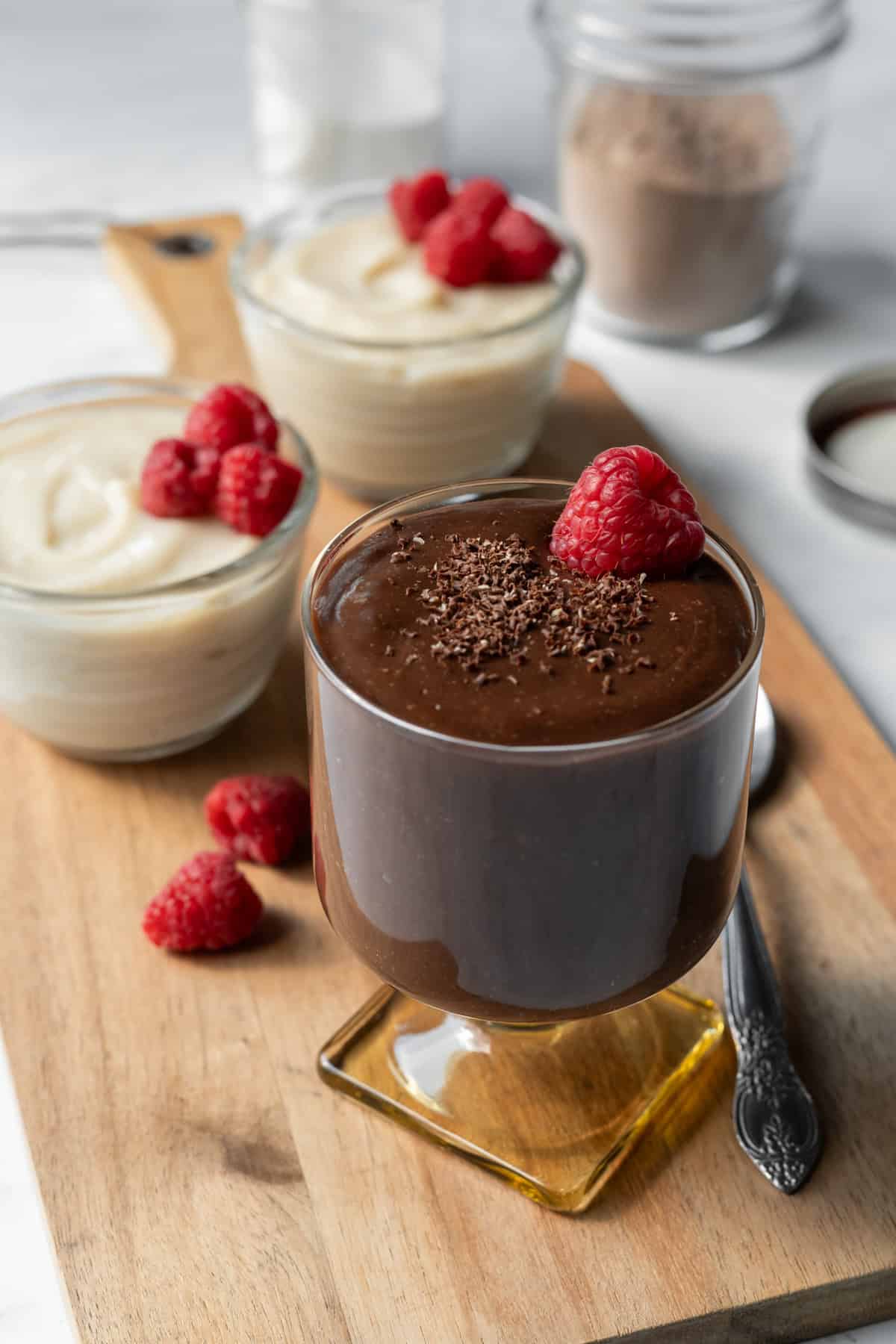 A parfait glass filled with vegan chocolate pudding topped with shaved chocolate and vanilla pudding in background.