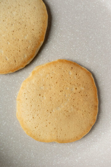 Two golden brown vegan pancakes on a non-stick griddle.
