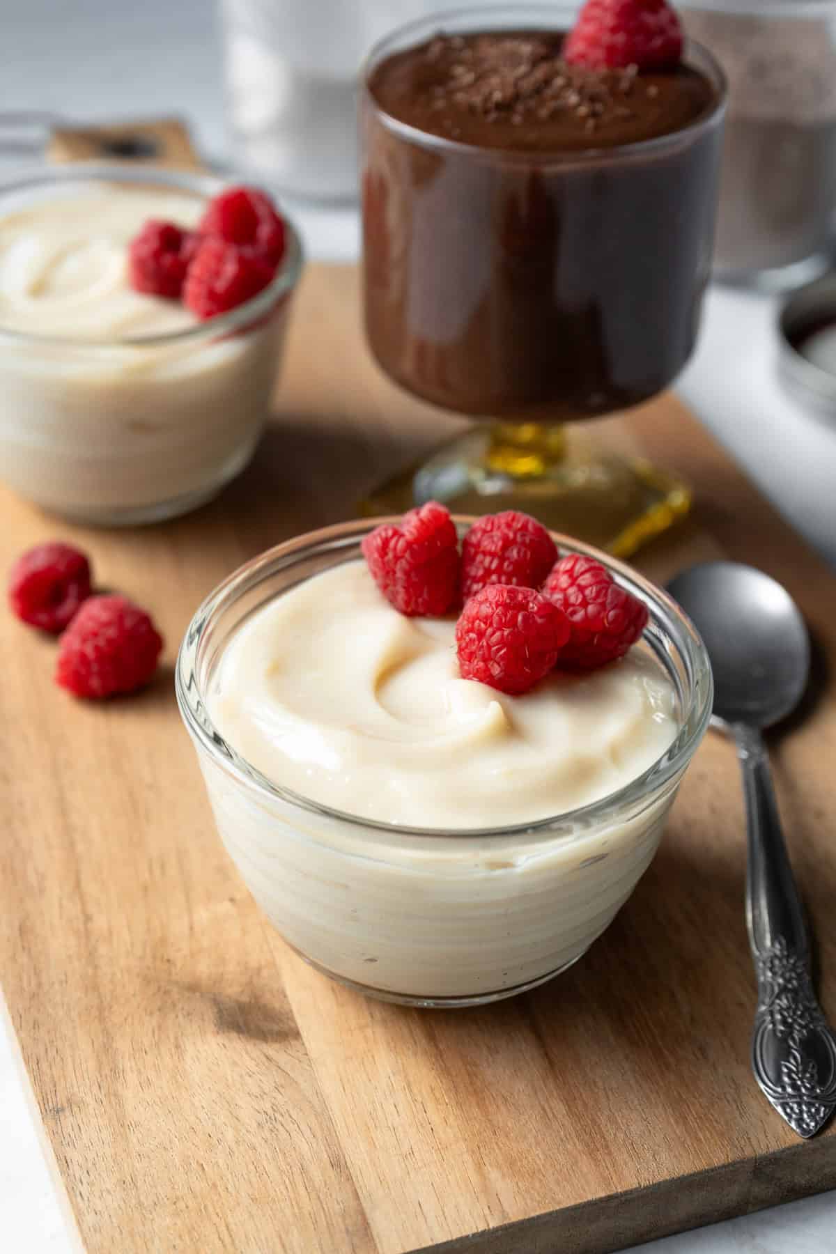 Individual servings of homemade chocolate and vanilla pudding garnished with raspberries.