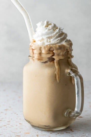 A frosty glass filled with homemade instant espresso frappe and topped with whipped cream.