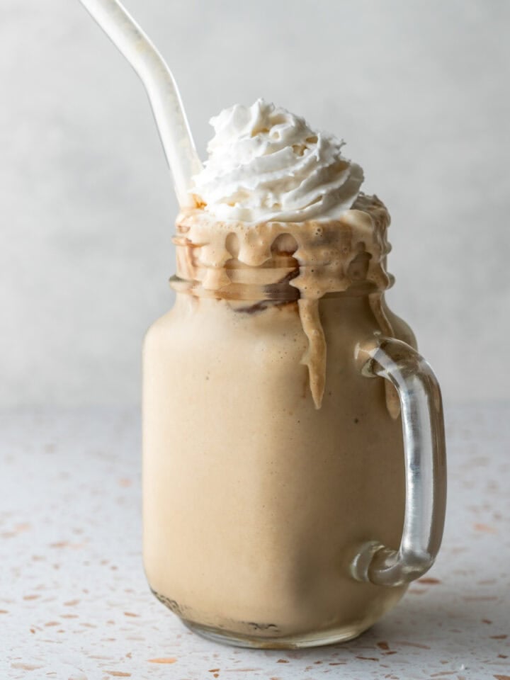 A frosty glass filled with homemade instant espresso frappe and topped with whipped cream.
