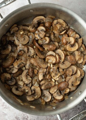 Adding garlic and herbs to the sauteed mushrooms.