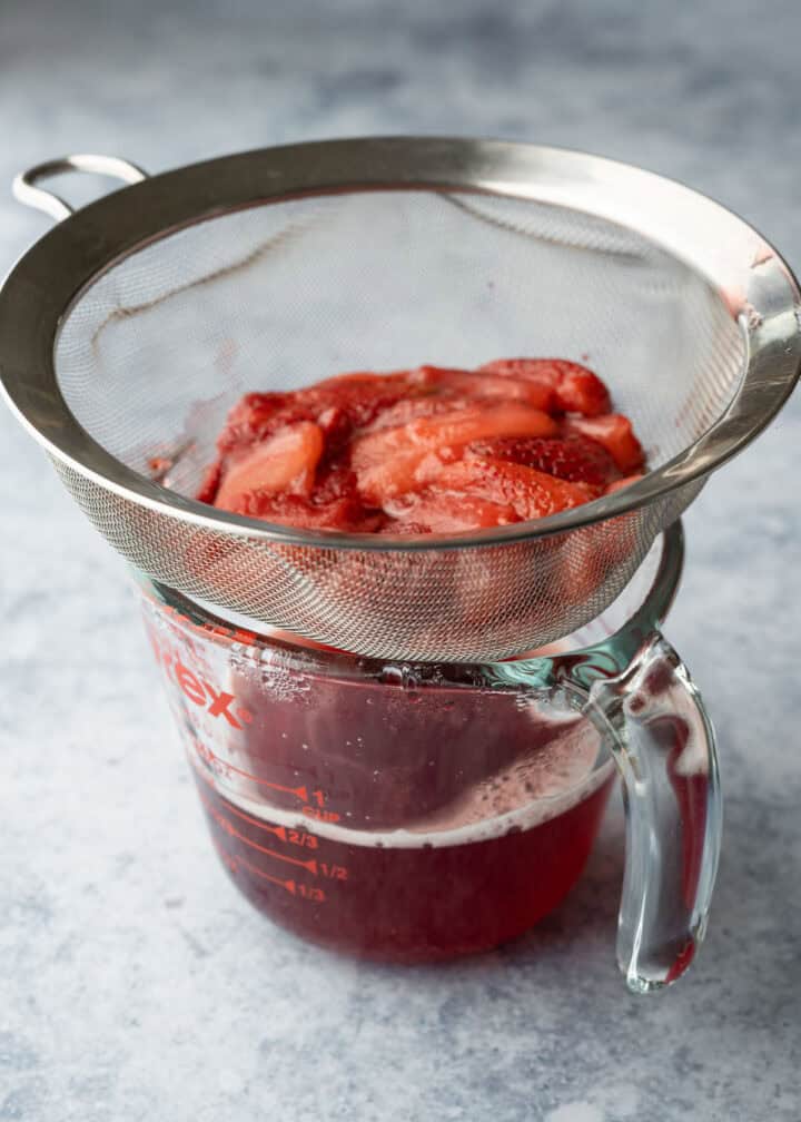 Straining homemade strawberry syrup into a glass measuring cup.