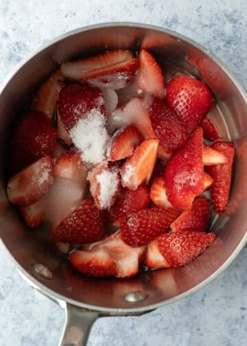 Quartered strawberries, sugar, and water in a small pot.