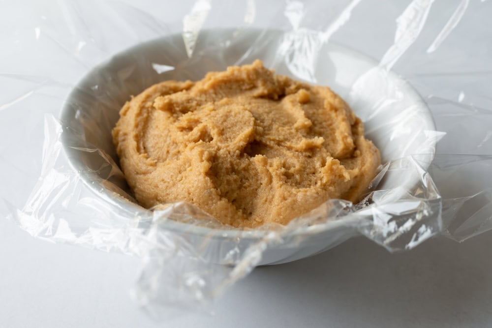 Freshly blended cashew cheese mixture resting in a bowl lined with plastic wrap.