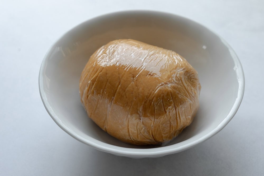 The cheese ball wrapped in plastic resting in a bowl.