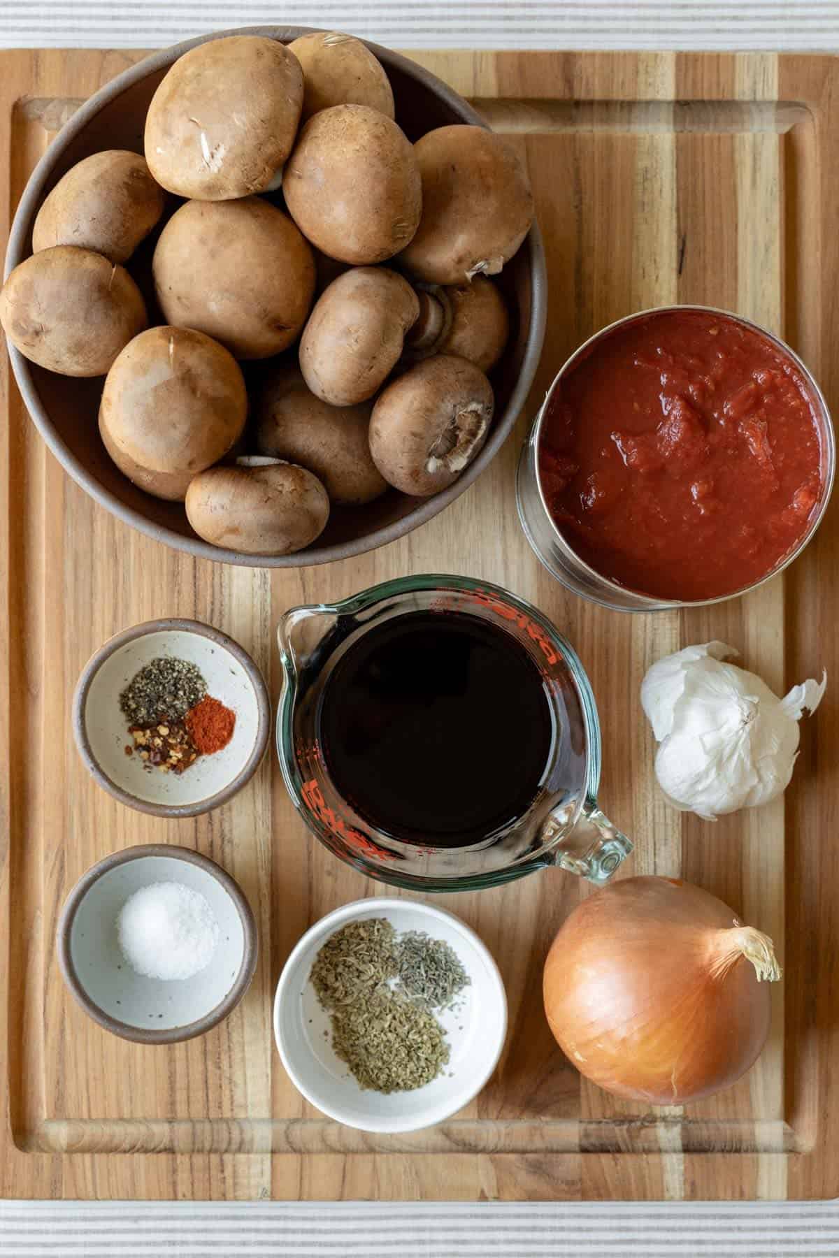 Ingredients needed to make mushroom ragu set out on a wood cutting board.
