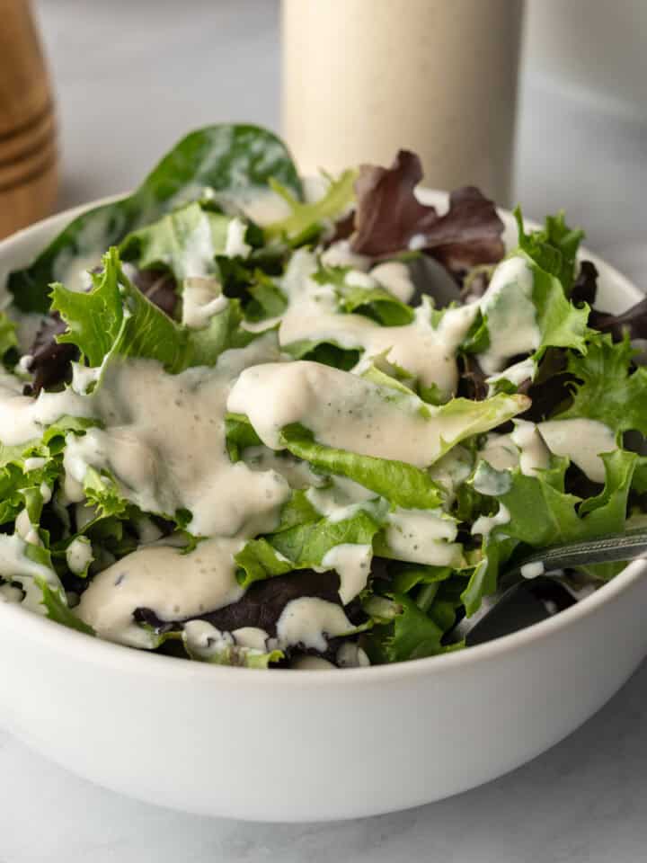 A bowl of mixed salad greens drizzled with creamy sweet onion dressing.