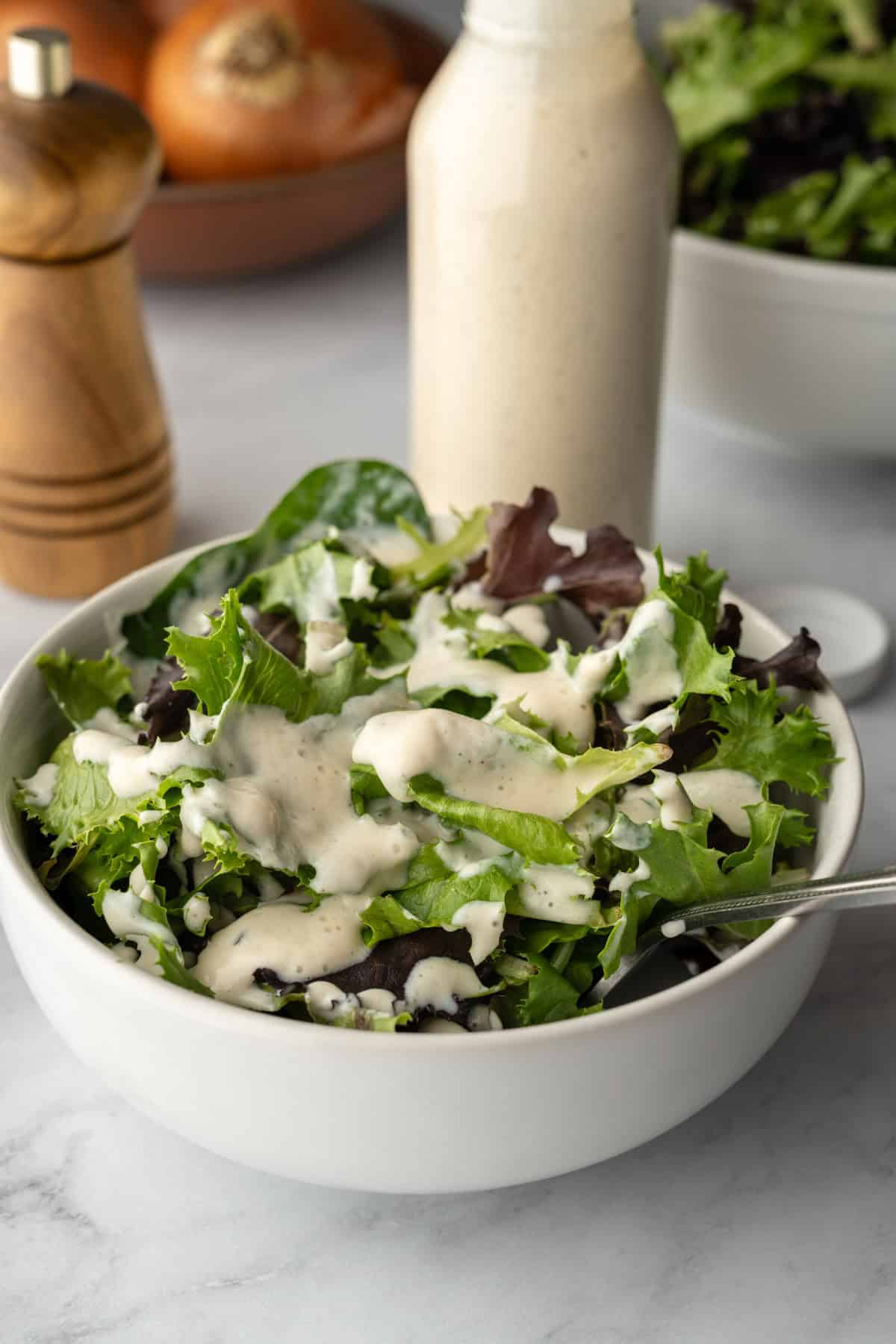 Salad in a white bowl with a jar of homemade dressing in the background.