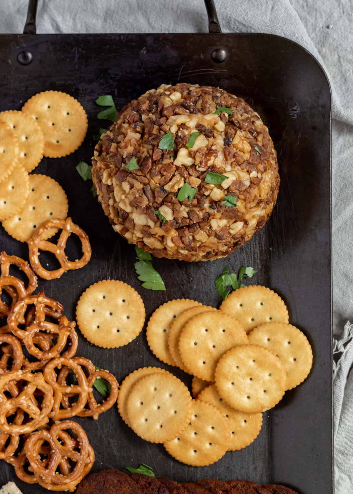 A vegan cheese ball on a black platter with crackers and pretzels.