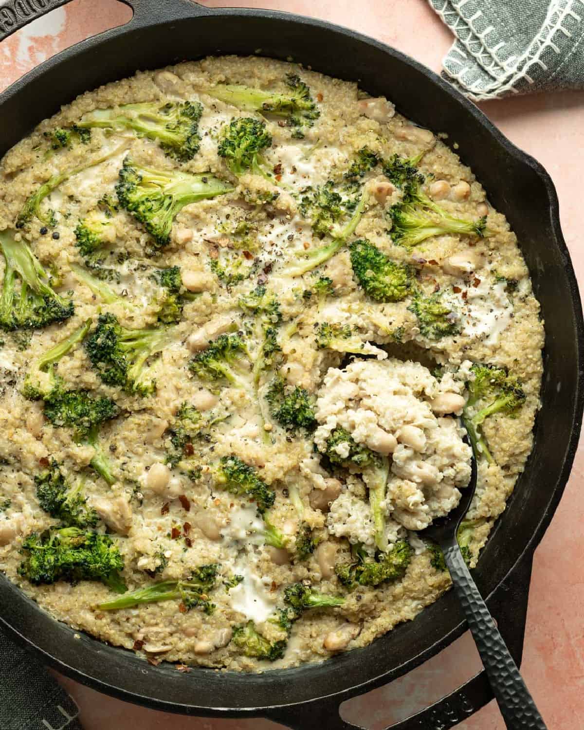 A skillet of broccoli quinoa casserole with dollops of homemade dairy free cheese on top.