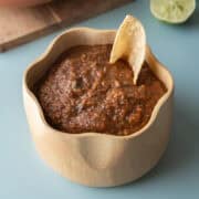 A bowl of homemade roasted salsa on a blue background.
