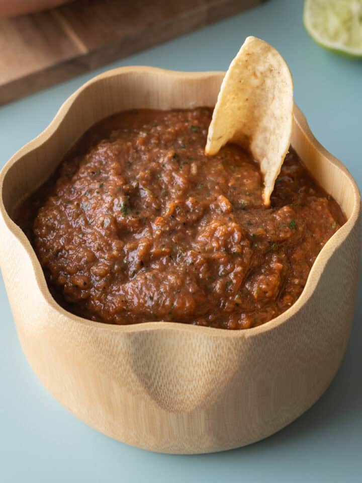 A bowl of homemade roasted salsa on a blue background.