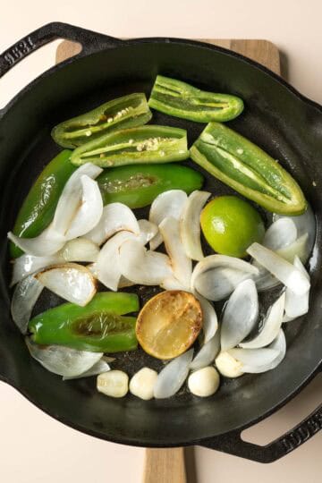 Showing light browning on cut lime halves, jalapeno, and onion in a large skillet.