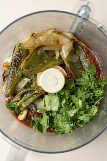 All of the salsa ingredients inside the bowl of a food processor.