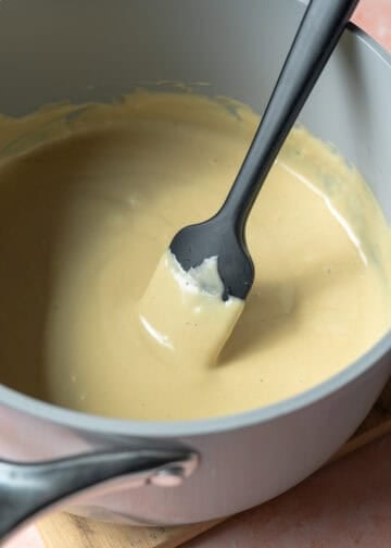 Simmering non-dairy milk and cheese powder on the stove until thickened and creamy.