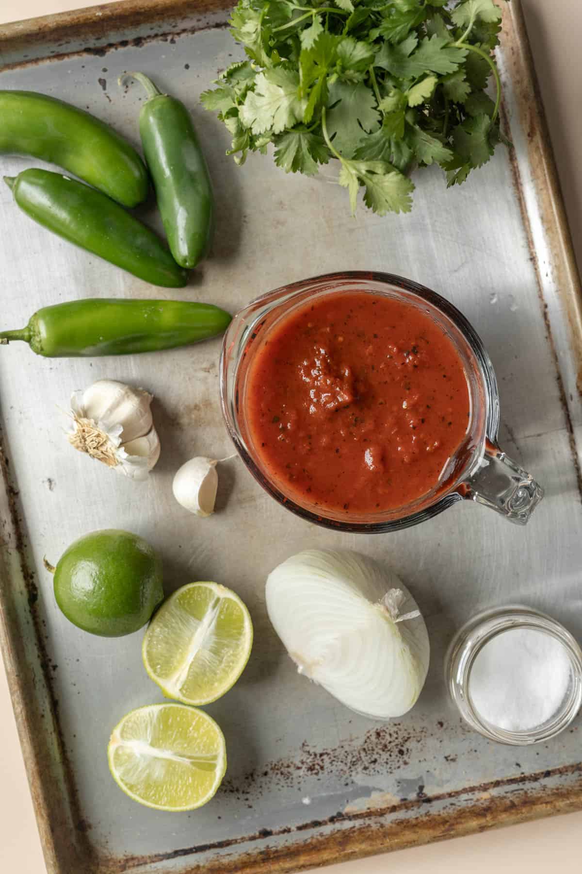 Fresh cilantro, jalapeno, onion, garlic, and lime plus canned tomatoes set out on a tray.