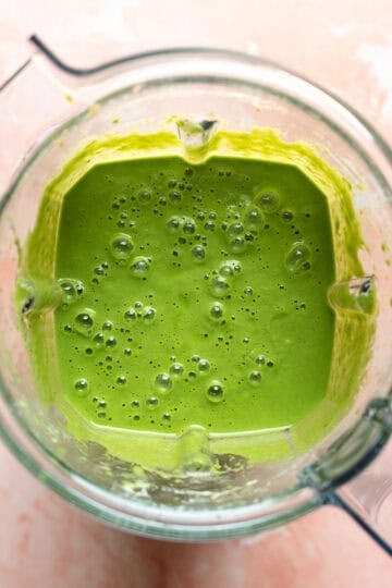 Looking inside a blender at bright green goddess sauce.