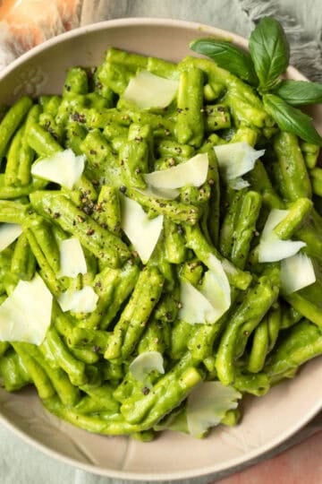 A large bowl filled with creamy green goddess pasta topped with shaved vegan Parmesan.