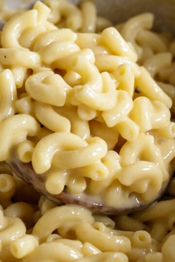 Spooning up extra creamy vegan mac and cheese from a pot.