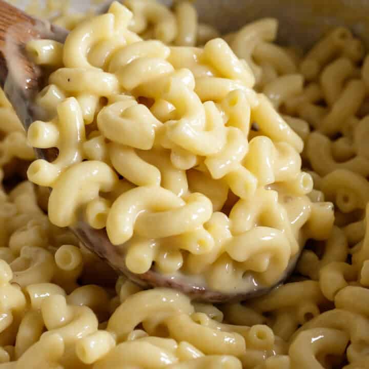 Spooning up extra creamy vegan mac and cheese from a pot.