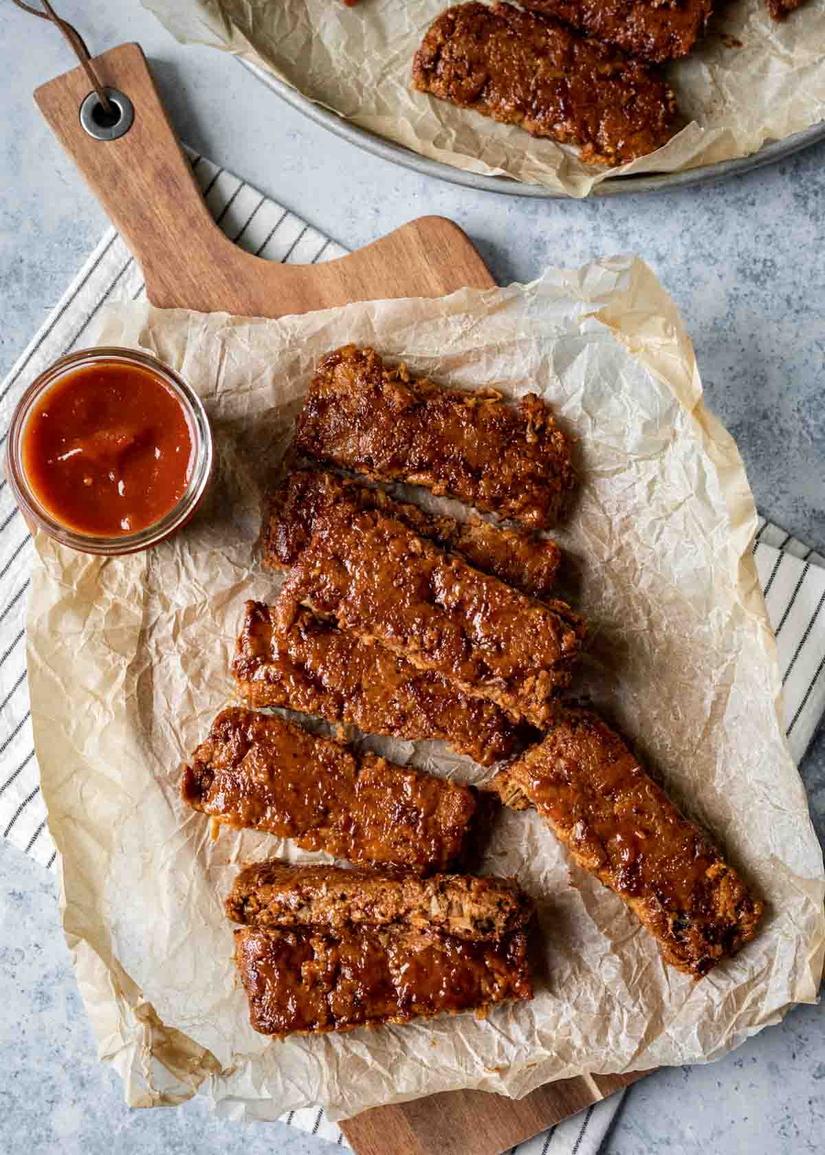 Seitan ribs coated in BBQ sauce resting on parchment paper.