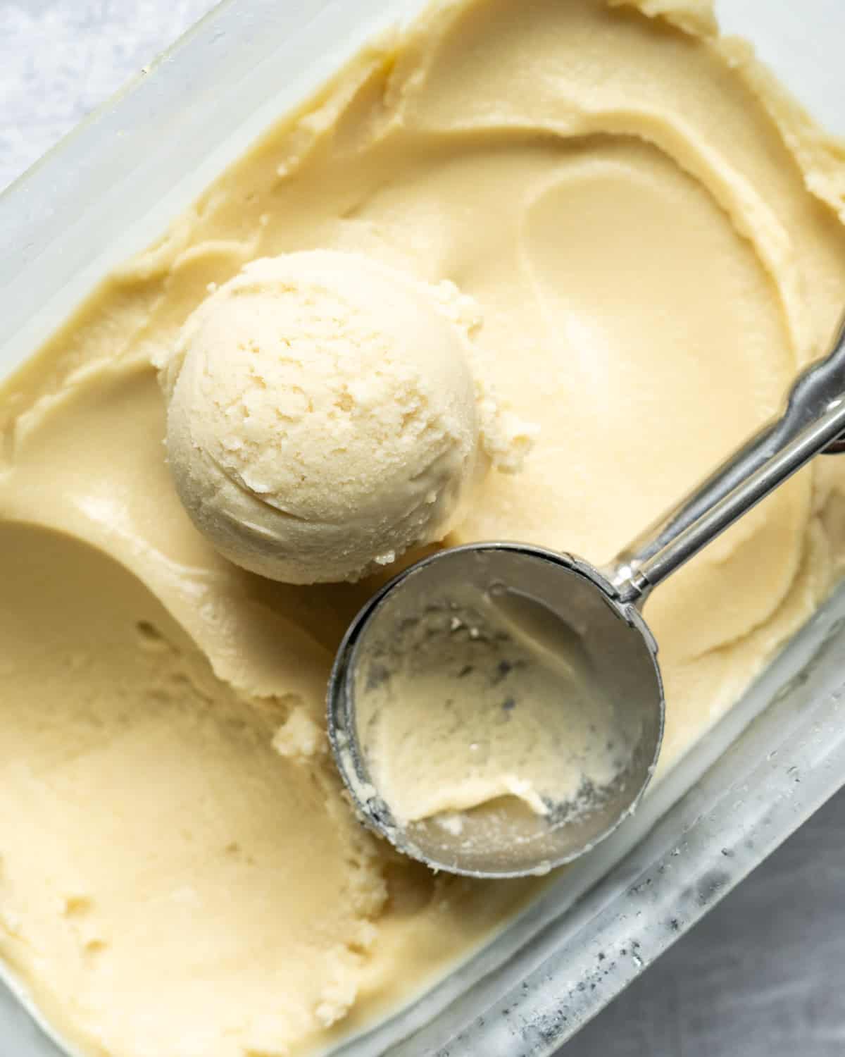 Overhead view of a pan of corn ice cream with a scoop resting on top.