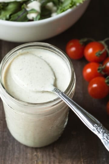 A jar of homemade pepperoncini dressing with a spoon showing creamy texture.