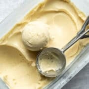 A scoop of vegan corn ice cream and a scooper resting on top of a pan full of ice cream.