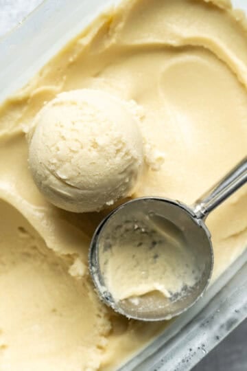 A scoop of vegan corn ice cream and a scooper resting on top of a pan full of ice cream.
