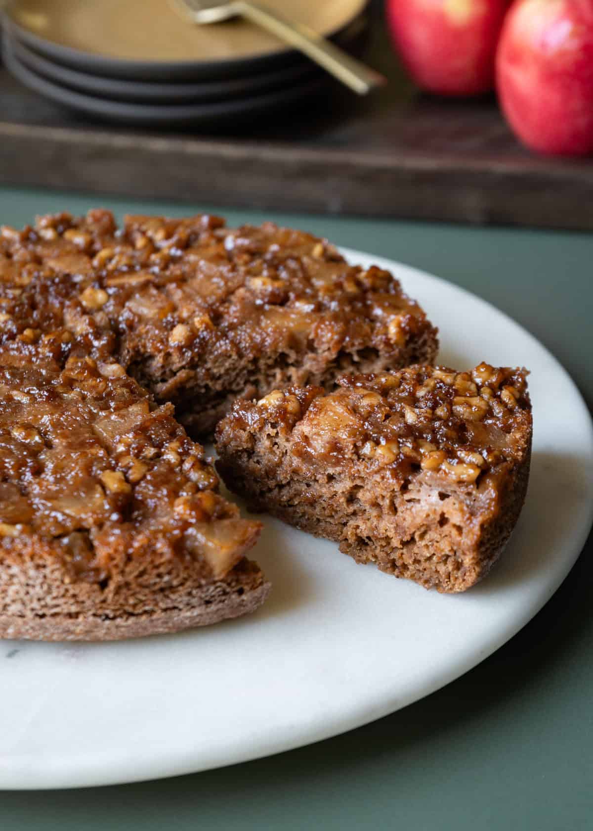 Upside down applesauce cake with gooey apple-walnuts on top resting on a white cake plate.