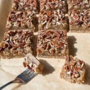 Sliced vegan pecan bars on parchment paper with a bite on a fork.