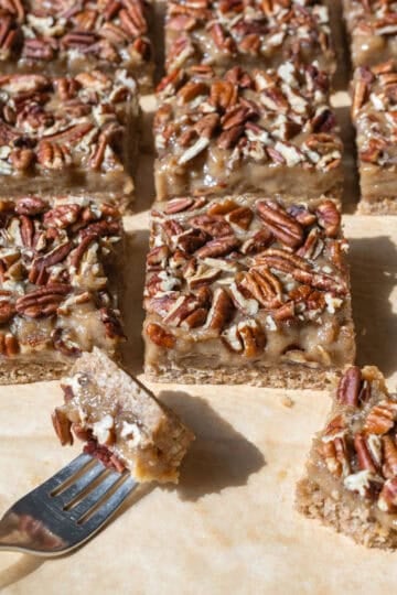 Sliced vegan pecan bars on parchment paper with a bite on a fork.