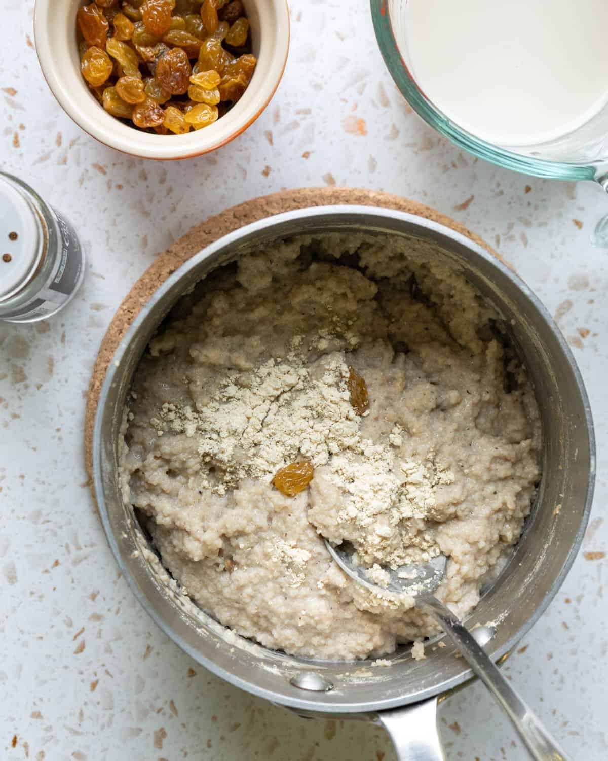 Adding non-dairy milk and protein powder to a small pot of cooked fonio.