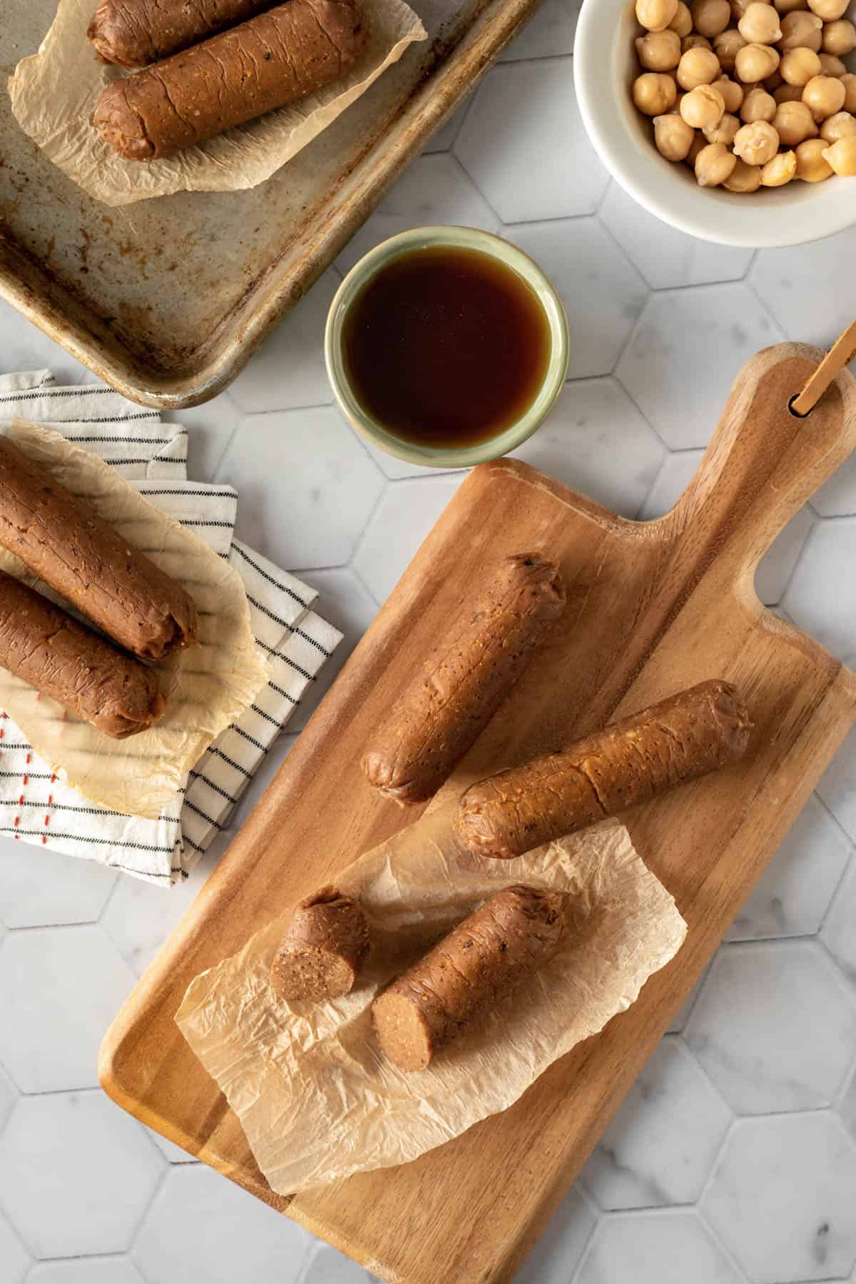 Instant Pot seitan breakfast sausages on a cutting board with chickpeas and maple syrup nearby.