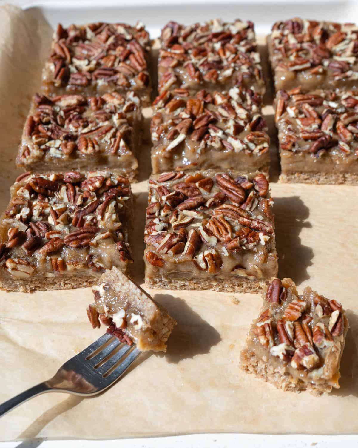 Pecan pie bars resting on a parchment-lined pan with a fork holding a bite.